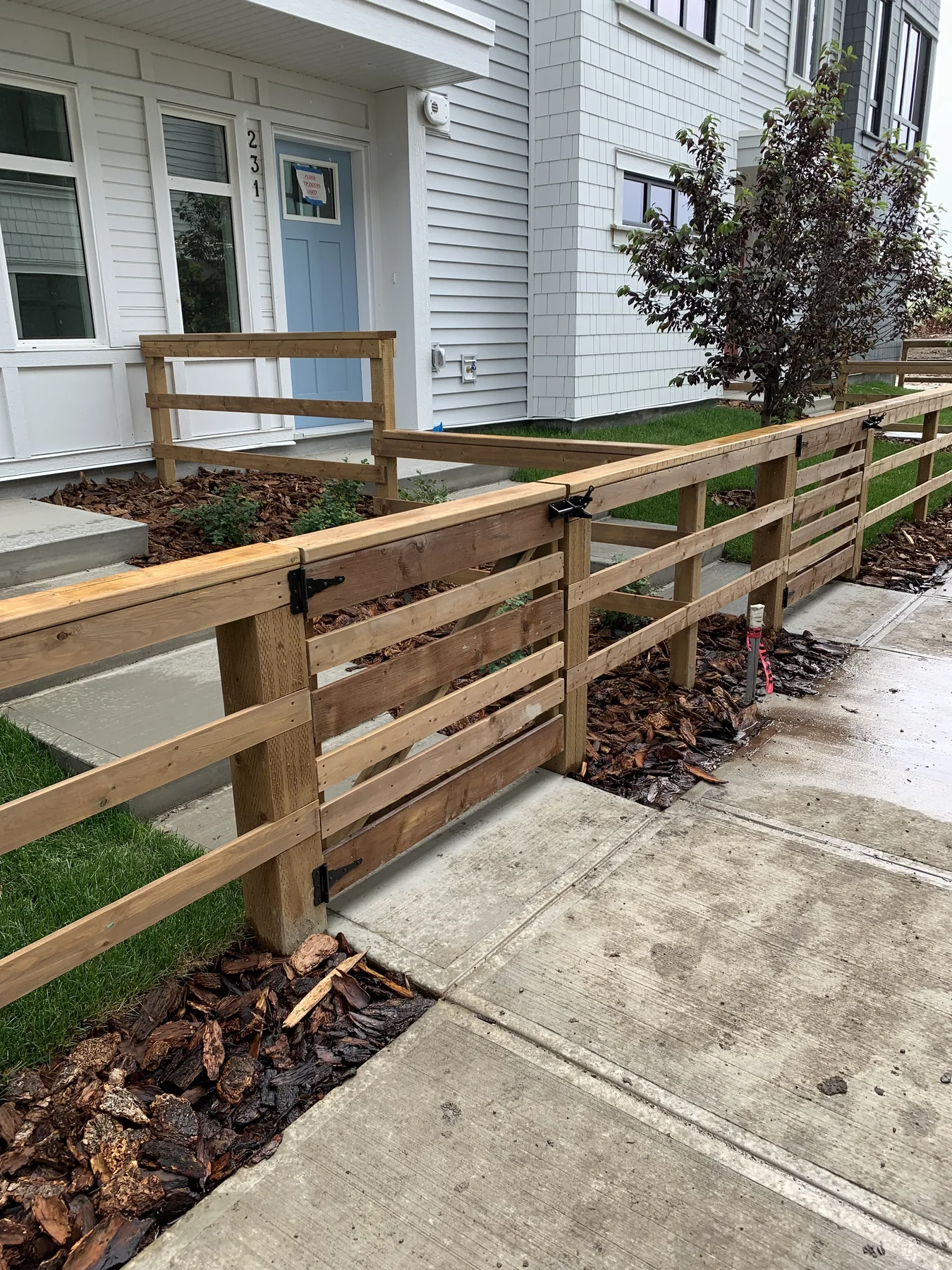 Wood entry fence with gates, mulch planting beds, and new green turf